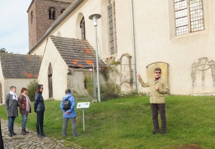 Man vor einer Kirche erläutert, daneben steht eine Infotafel. 